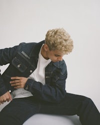 a young man in a denim jacket sitting on the ground