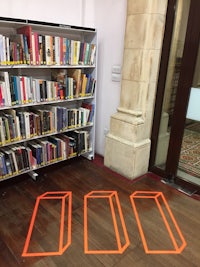 three orange lines on the floor in front of a bookshelf