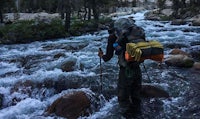 a hiker is crossing a river with a backpack