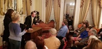 a man speaks to a group of people in an ornate room