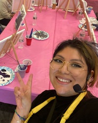 a woman holding a peace sign in front of a pink table