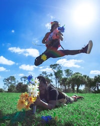 two people jumping in the grass with flowers in their hands