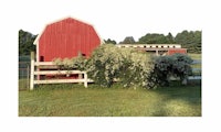a red barn with a white fence and bushes
