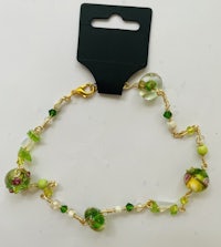 a bracelet with green glass beads and a gold tag
