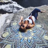 a woman laying on a rock with a chalk drawing of a mandala
