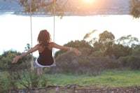 a woman swinging on a swing in front of a lake