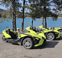 four polaris slingshots parked next to a lake