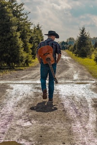 a man walking down a dirt road with a guitar