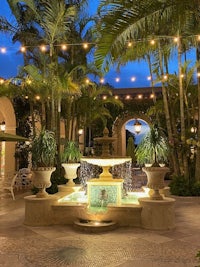 a courtyard with a fountain and palm trees at dusk