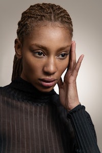 a black woman with dreadlocks posing with her hand on her face