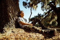 a man sitting under a tree with a skateboard