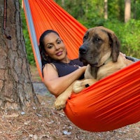 a woman laying in an orange hammock with her dog