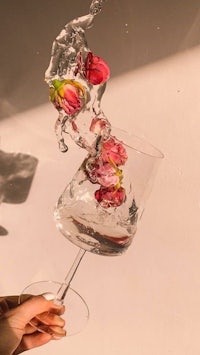 a person is holding a glass of water with flowers in it
