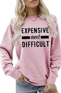 a woman wearing a pink sweatshirt that says expensive and difficult