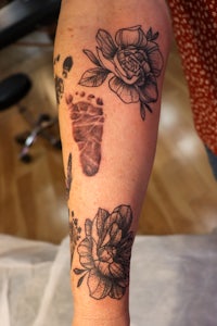 a woman's arm tattooed with flowers and footprints