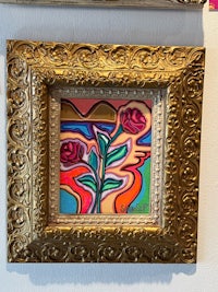 a gold framed painting of a rose on a wall