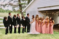 a group of bridesmaids and groomsmen posing in front of a barn