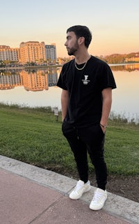 a man standing in front of a lake wearing a black t - shirt and sneakers