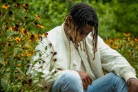 a man with dreadlocks sitting in a field of flowers