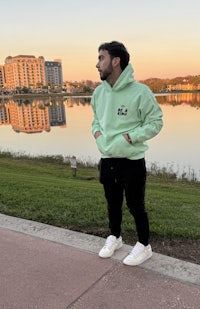a man standing in front of a lake wearing a green hoodie