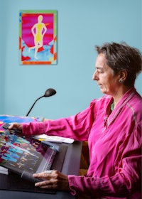 a woman in a pink shirt sitting at a desk with a laptop