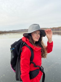 a woman in a red jacket and hat standing near a body of water
