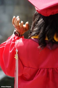 a woman in a red graduation gown is holding a tassel