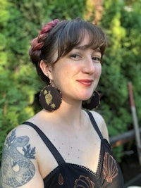 a woman with tattoos wearing a black dress and earrings