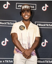 a young man wearing a hat and a t-shirt standing in front of a black tik tok sign