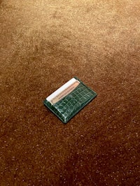 a green crocodile leather card holder on a brown floor