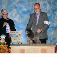 a man and woman standing next to a poodle at a dog show