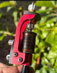 a hand holding a red and black tattoo machine
