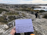 a person is holding a drawing of a landscape on a rock