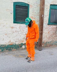 a man in an orange tracksuit standing next to a brick wall