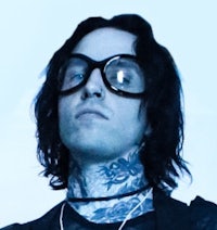 a man with tattoos and glasses is standing in front of a blue background