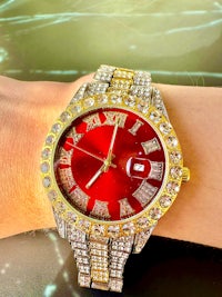 a woman's wrist with a red and gold watch