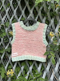 a pink and green knitted sweater on a metal fence