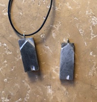 two silver pendants on a black leather cord