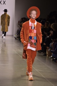 a man walking down the runway in an orange suit and hat