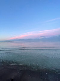 a beach at sunset with a pink sky and water