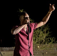 a man in a maroon shirt singing into a microphone