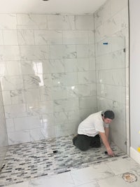 a man is kneeling on the floor of a tiled shower