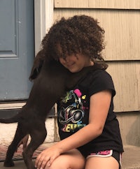 a little girl hugging a brown puppy