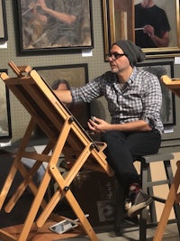 a man sitting on an easel in front of paintings