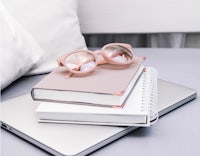 a notebook, glasses and a laptop on a bed
