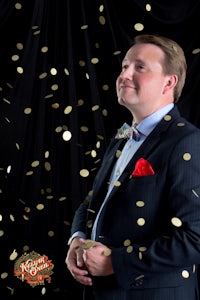a man in a suit standing in front of gold confetti