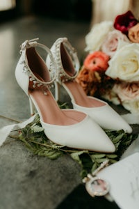 a pair of white wedding shoes and a bouquet of flowers