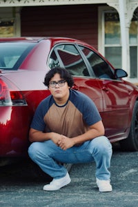 a man crouching next to a red car
