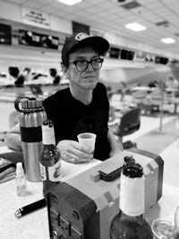 a black and white photo of a man sitting at a bowling alley