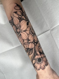 a black and white tattoo of flowers on the forearm